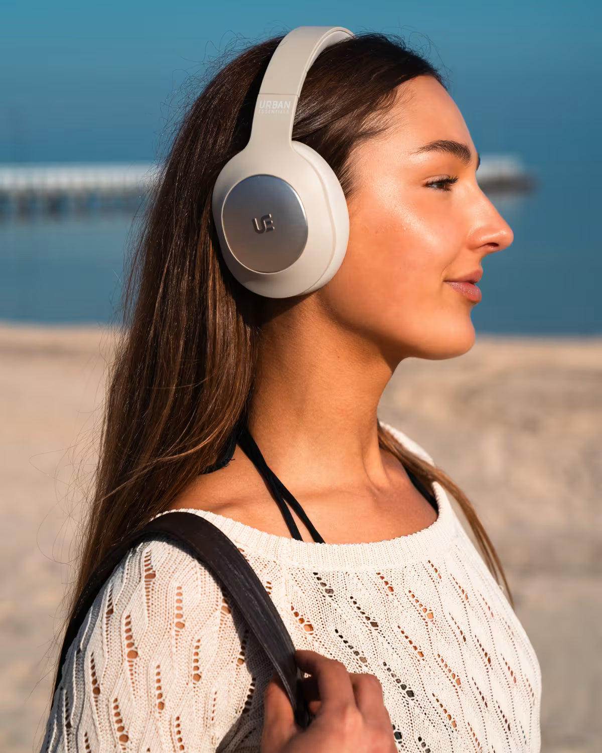 A women on the beach wearing the Urban Essentials beige FLOW headphones.
